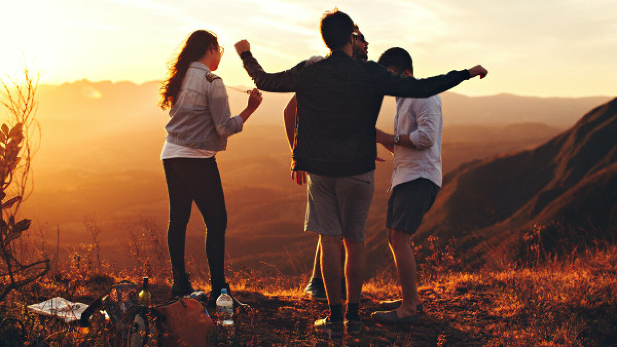 Four Person Standing at Top of Grassy Mountain