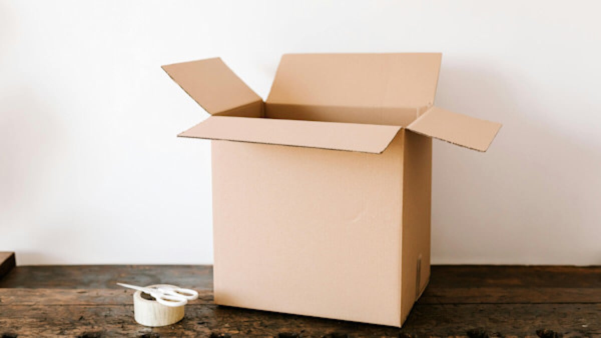 Cardboard box on dark wooden table near tape and scissors